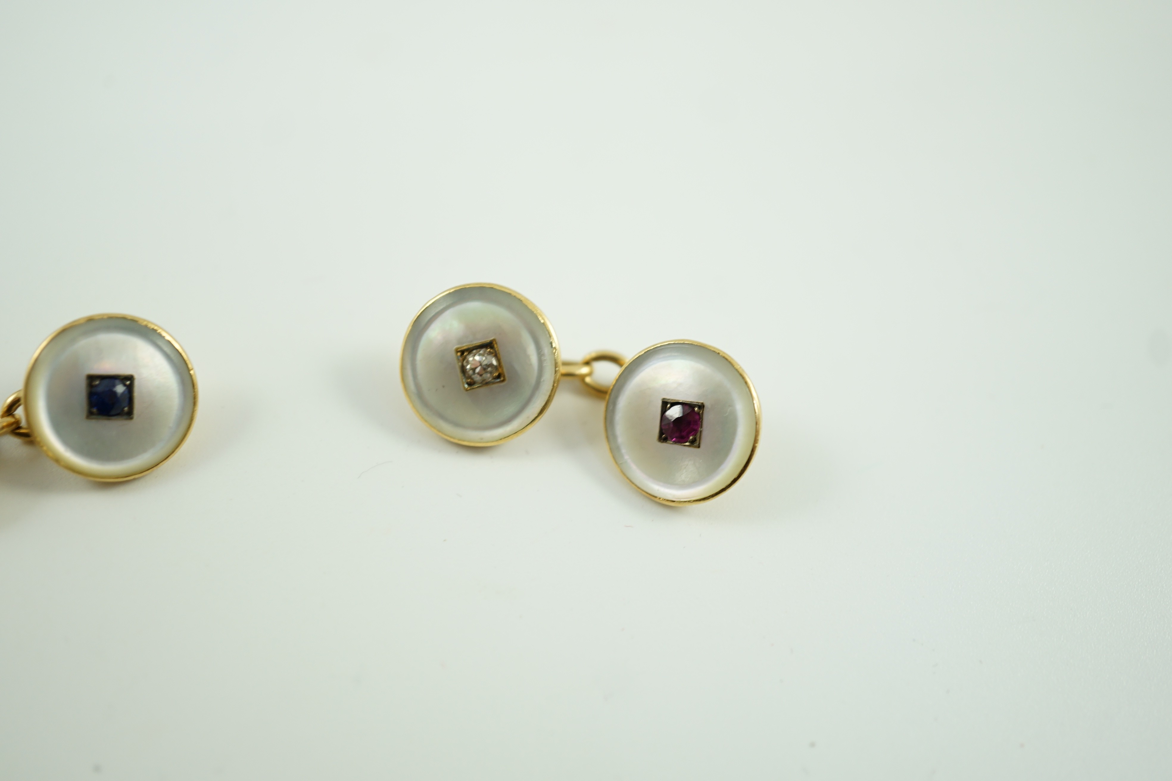 A pair of early to mid 20th century yellow metal mounted mother of pearl and gem set cufflinks, one set with a ruby and diamond, the other with a sapphire and diamond, link diameter 12mm, gross weight 8 grams.